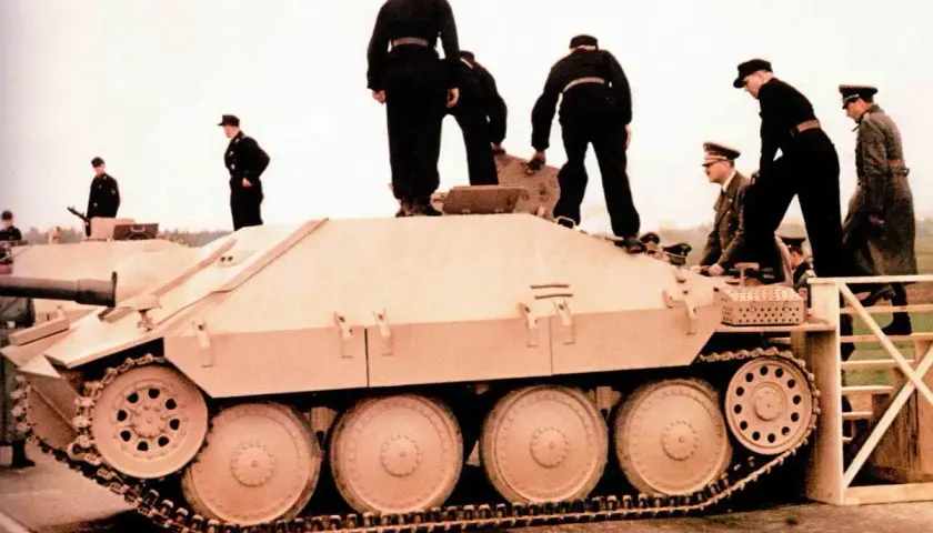 Männer in Uniformen stehen auf und neben einem hellbraunen Opel Hetzer Jagdpanzer.