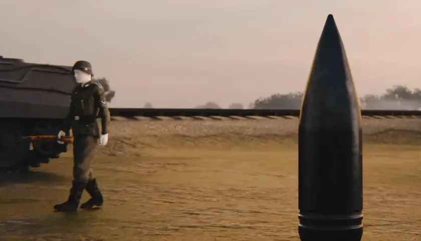 Ein Soldat geht an einer riesigen Kugel vorbei, die schwerer Gustav Munition darstellt. Im Hintergrund ist eine Eisenbahnlinie zu sehen.
