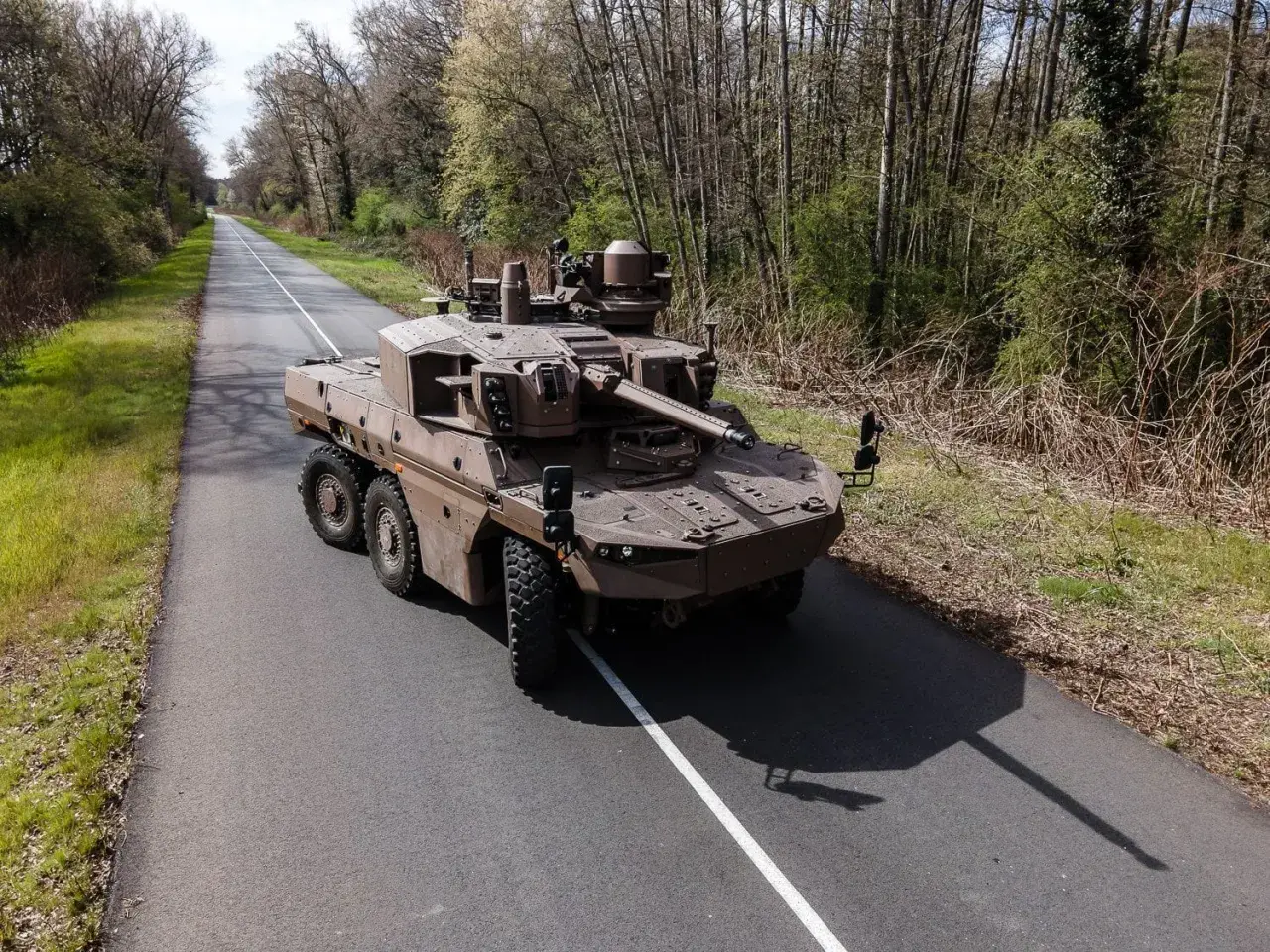 Ein moderner Jaguar-Panzer, ein stolzes Stück Militärtechnik aus Frankreich, fährt auf einer einsamen Straße durch bewaldetes Gebiet.