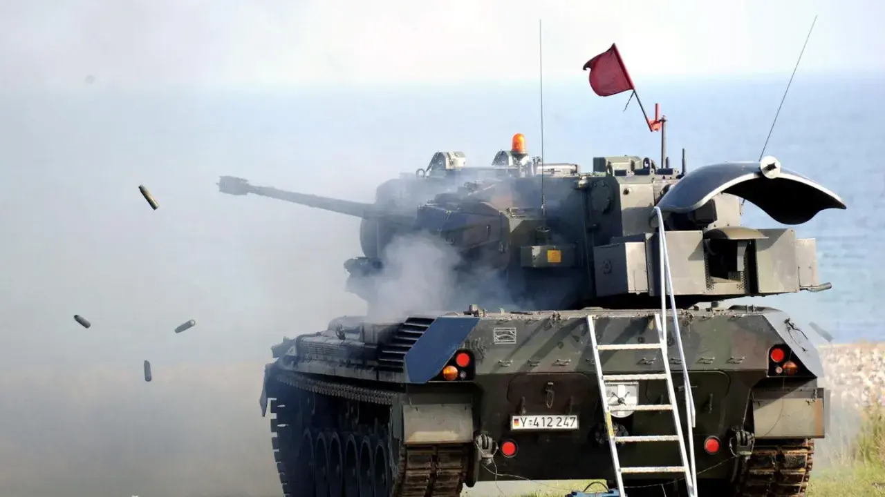 Ein Flakpanzer 1 feuert, Patronenhülsen fliegen durch die Luft. Rauch steigt aus dem Turm auf.