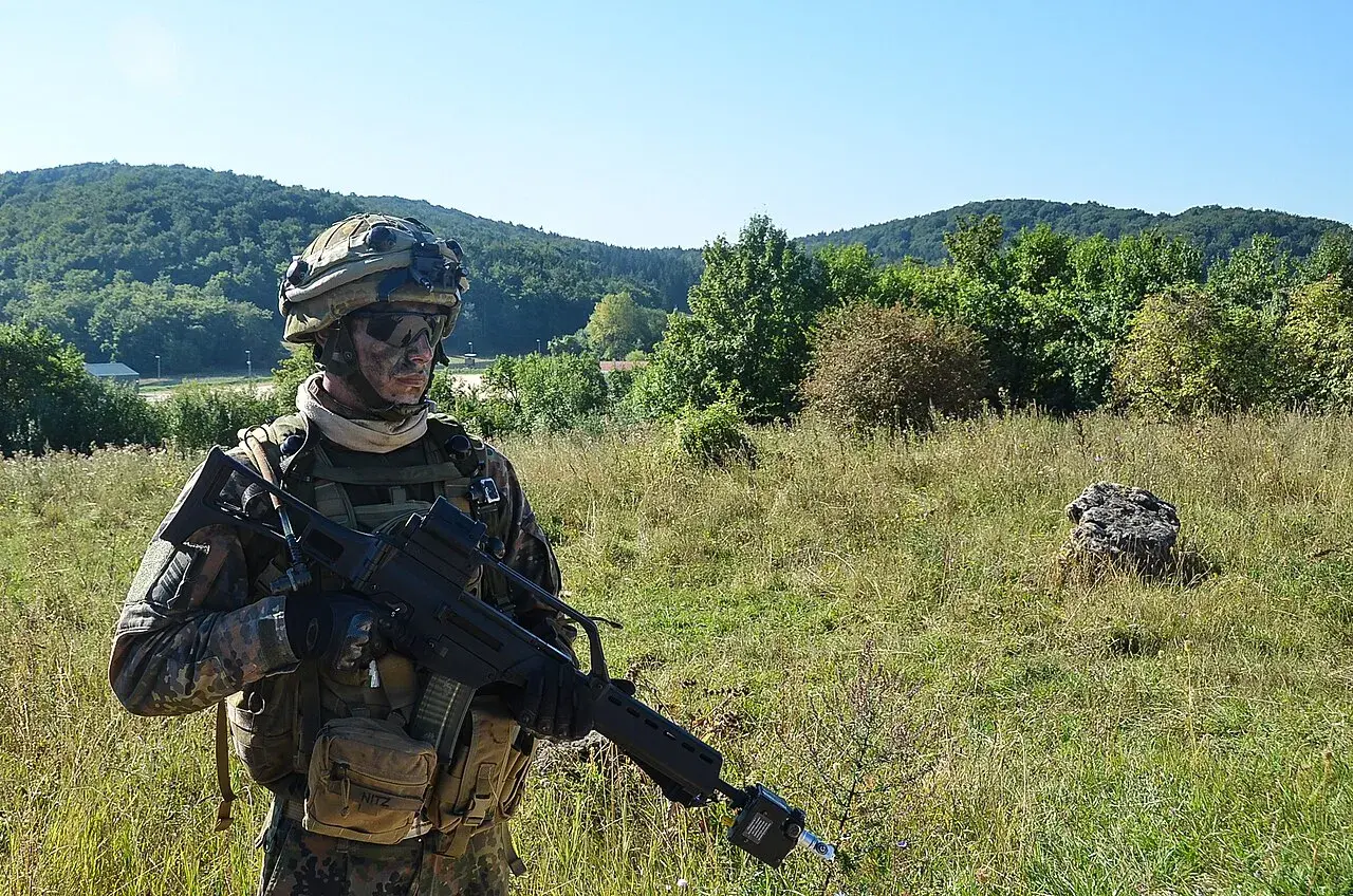 Soldat der Bundeswehr mit Tarnmuster und Gewehr im Feld. Die 5 Streifen auf seiner Ausrüstung sind kaum zu erkennen.