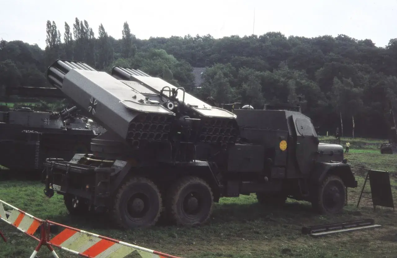 Lars Panzer, ein Raketenwerfer auf einem LKW, steht im Gras. Im Hintergrund ein Panzer.