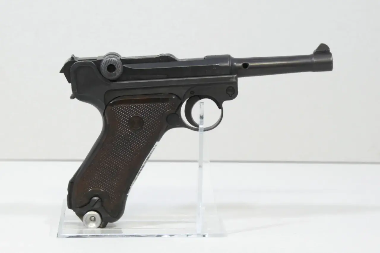 Eine schwarze Luger P08 Wehrmacht Pistole mit braunen Griffschalen, auf einem transparenten Ständer.