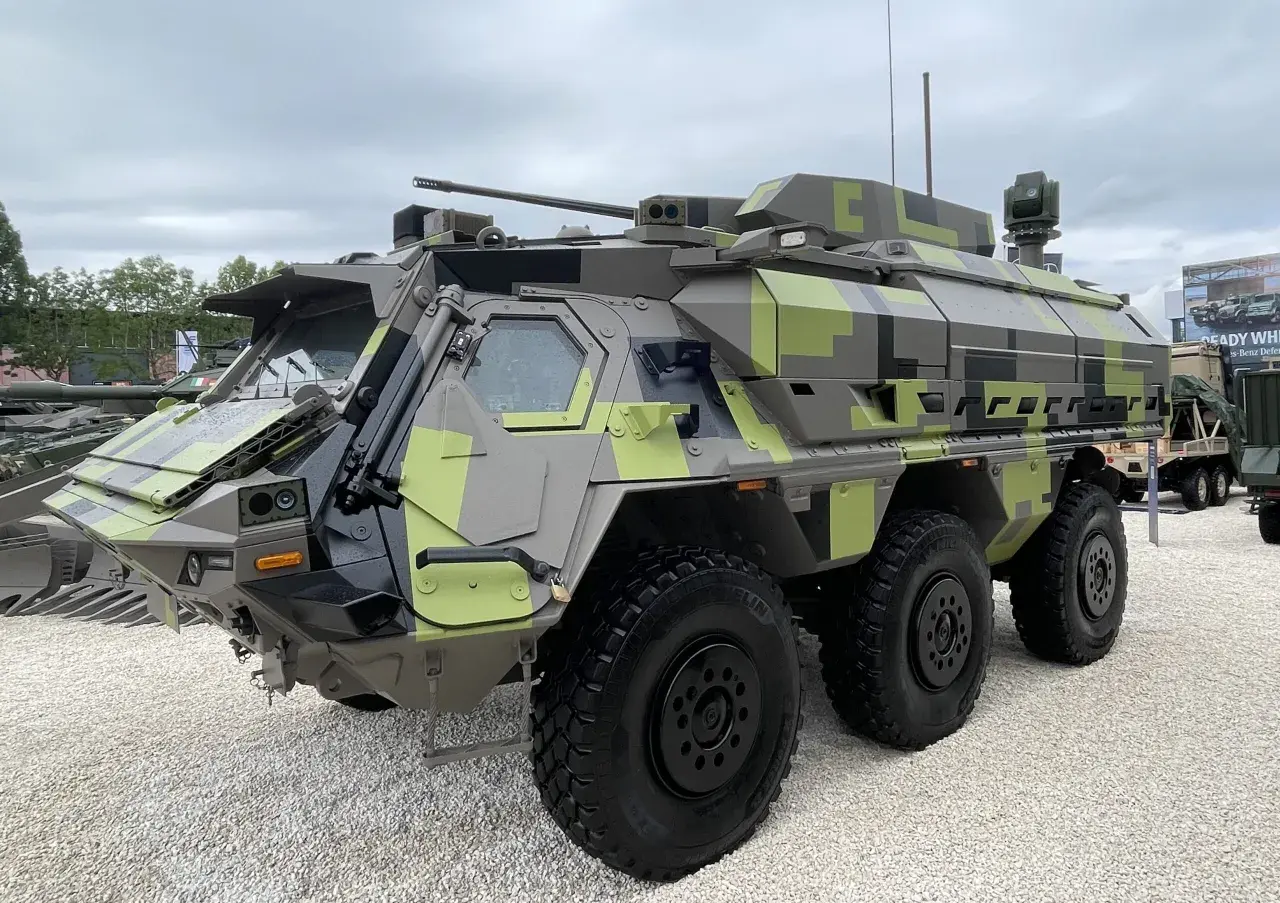 Ein gepanzertes Fahrzeug mit Tarnmuster, das als Fennek-Nachfolger präsentiert wird. Es verfügt über eine Waffenstation und mehrere Sensoren.