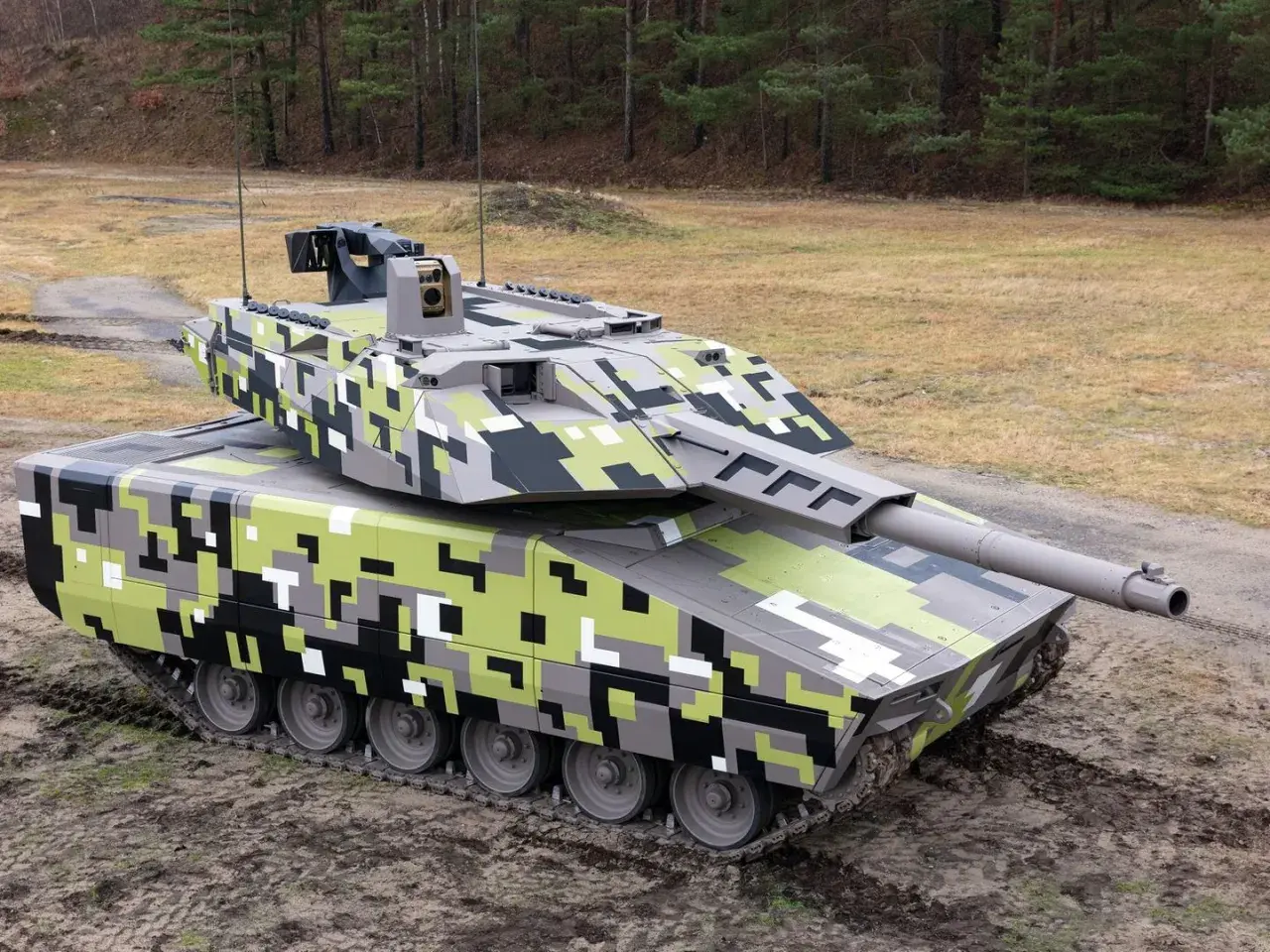Ein moderner Jagdpanzer mit digitaler Tarnung steht auf schlammigem Untergrund vor einem Wald.