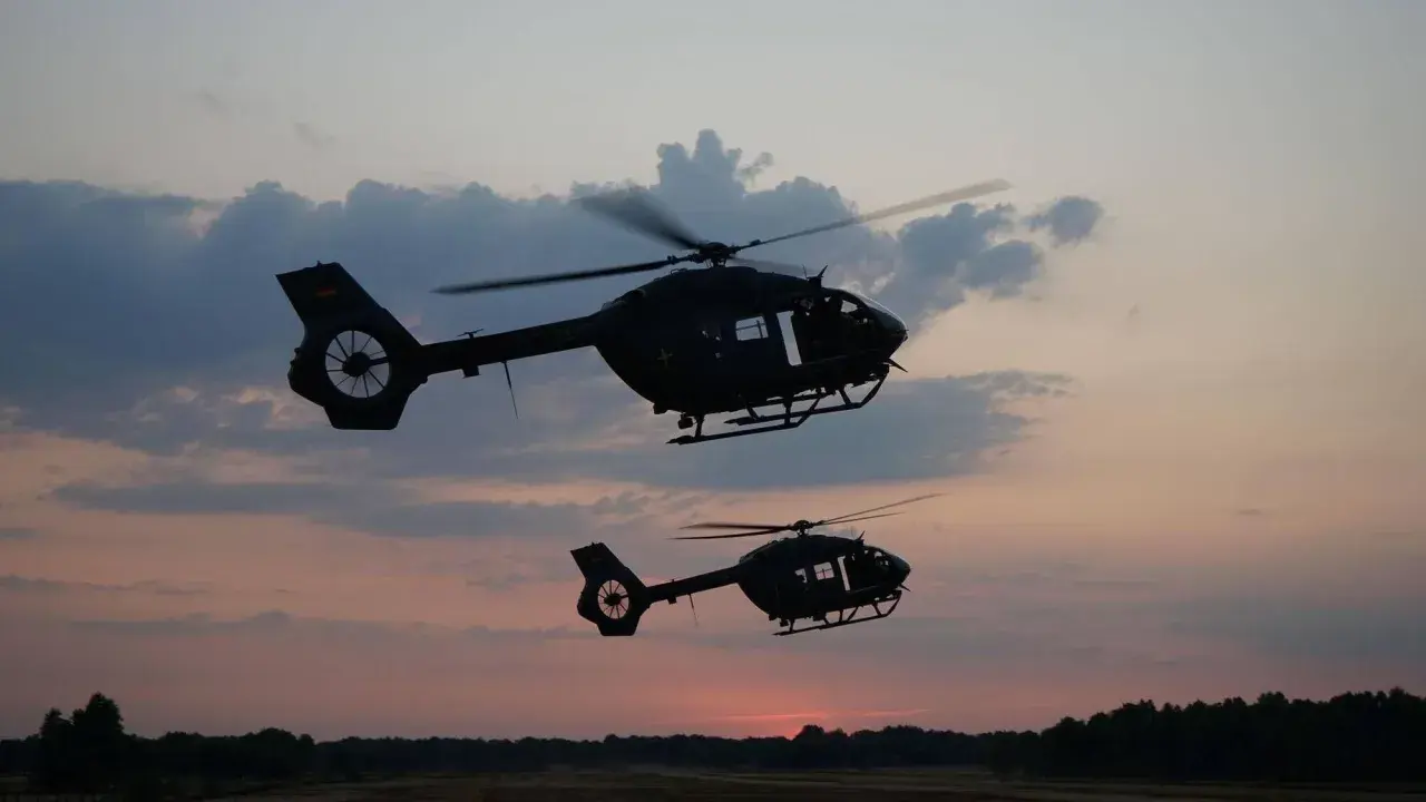 Zwei KSK Hubschrauber fliegen im Abendrot über eine Waldlandschaft.