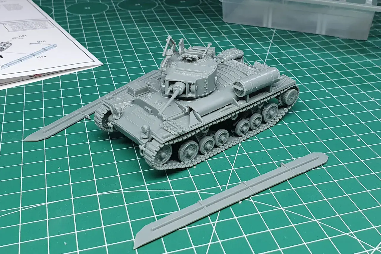 Ein grauer Modellbausatz eines Valentine Panzers liegt auf einer grünen Schneidematte. Zwei separate Panzerplatten liegen daneben.