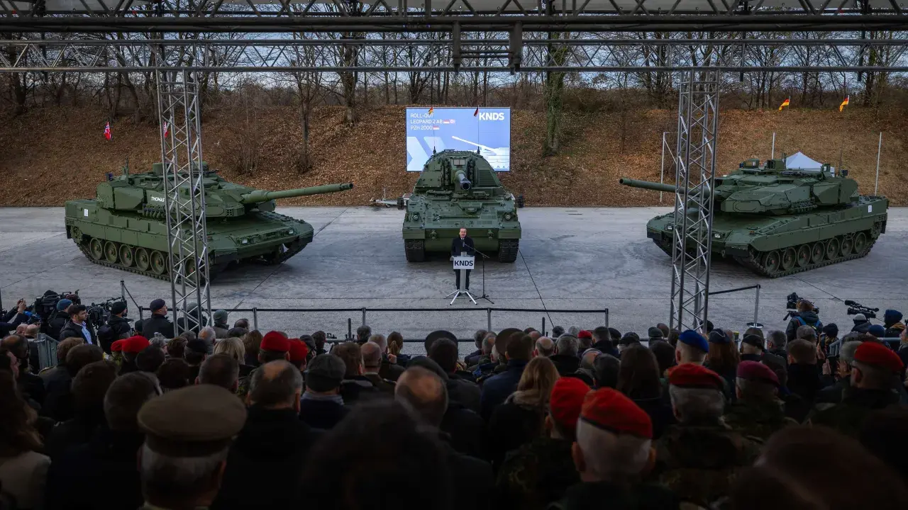 Drei Panzer, ein Redner und eine Zuschauermenge bei einer Veranstaltung.