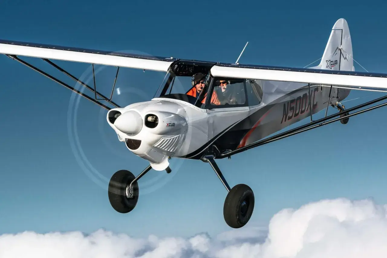 Zwei Piloten fliegen in einer CubCrafters X-Cub über den Wolken.