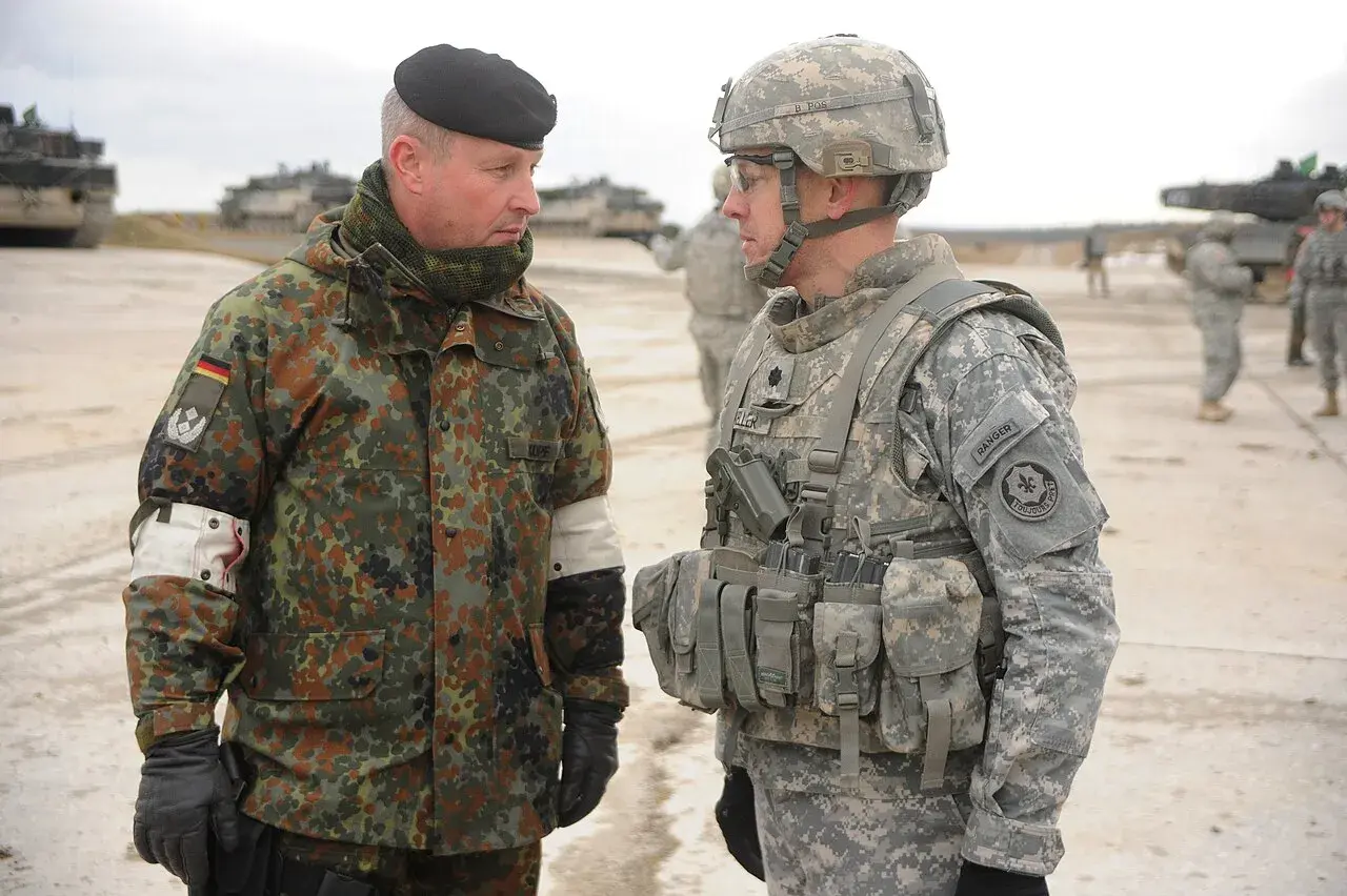 Zwei Soldaten im Gespräch, einer mit deutschem Tarnmuster und schwarzem Barett, der andere in US-Uniform. Der deutsche Soldat trägt den oberstleutnant dienstgrad.