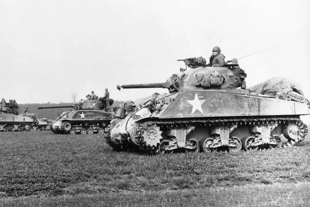 Mehrere Sherman-Panzer, einer mit der Aufschrift "Virgin", stehen auf einem Feld.