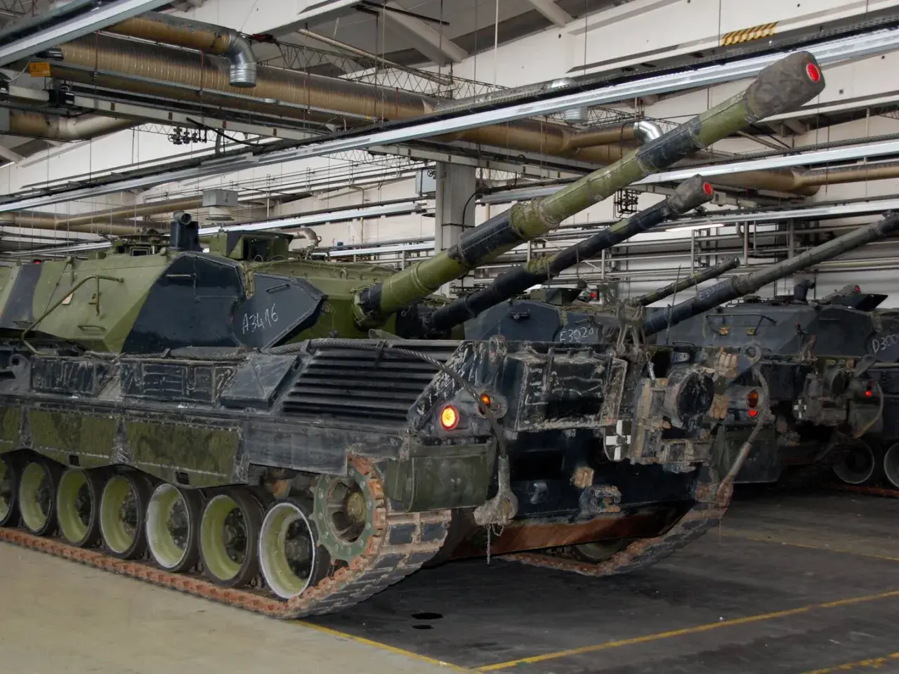Mehrere Leopard 1 Panzer stehen in einer Halle. Ihre Kanonen ragen nach oben.