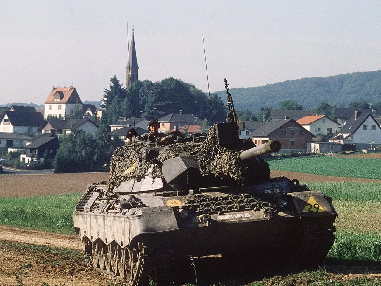 Ein Leopard 1 Panzer mit Tarnnetz fährt durch ein Feld. Die Munition ist bereit für den Einsatz.