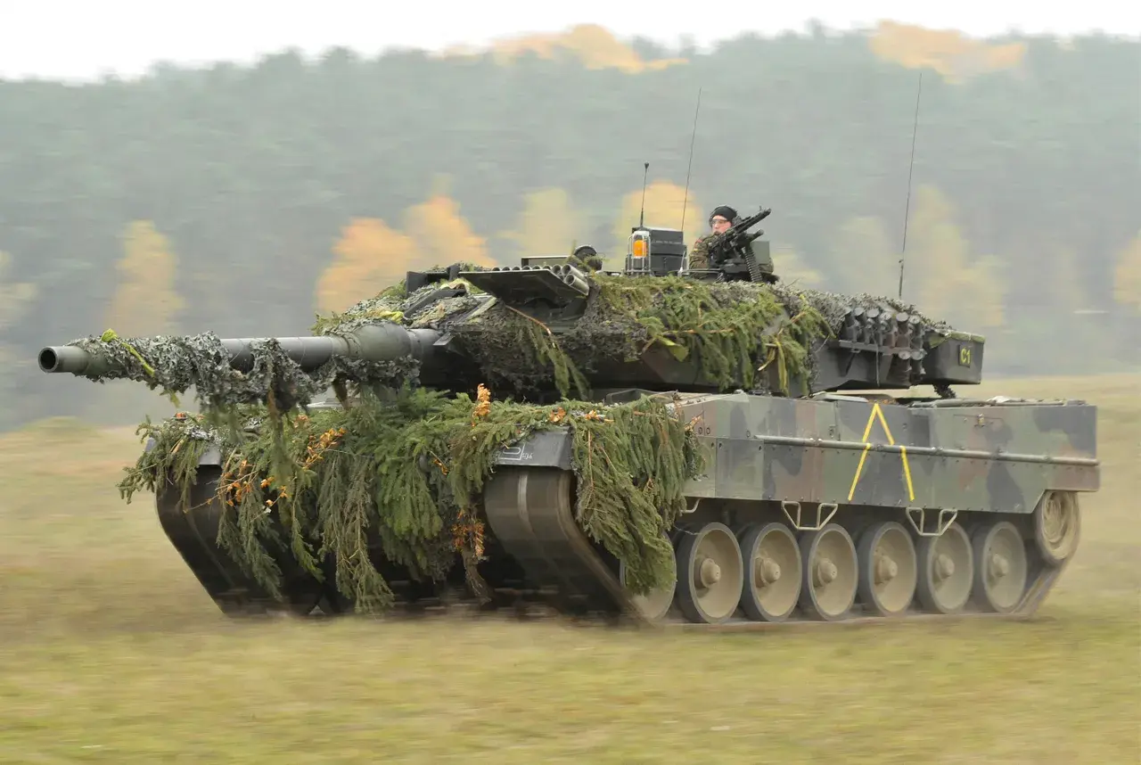 Ein getarnter Panzer Leopard 2 fährt durch herbstliches Gelände. Er sieht aus wie aus einem modernen Weltkrieg.