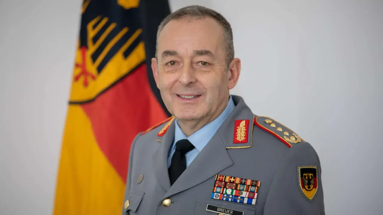 Ein Mann in Uniform mit einem Generalmajor-Abzeichen, vor der deutschen Flagge.
