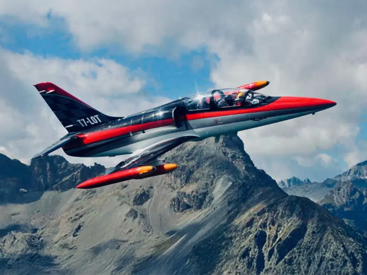 Ein rotes und graues Düsenflugzeug, das wie ein Albatros aussieht, fliegt über felsige Berge.