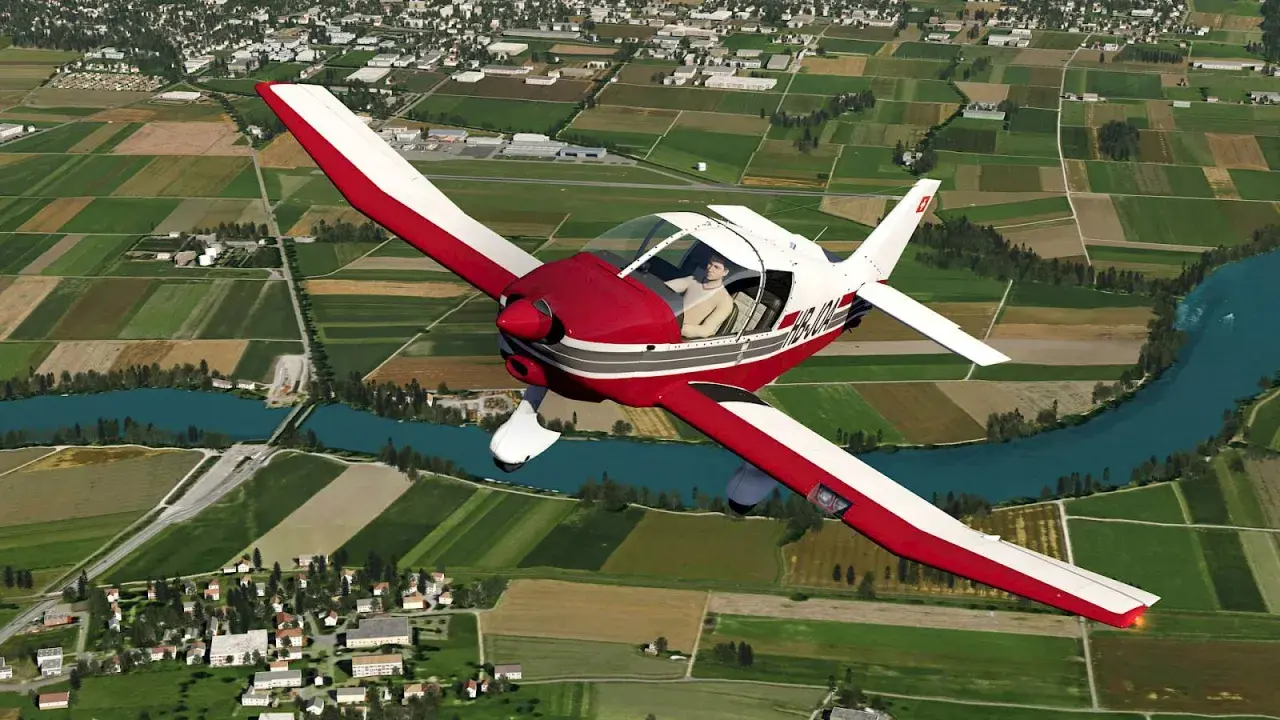 Ein roter und weißer Robin DR 400 fliegt über grüne Felder und einen Fluss.