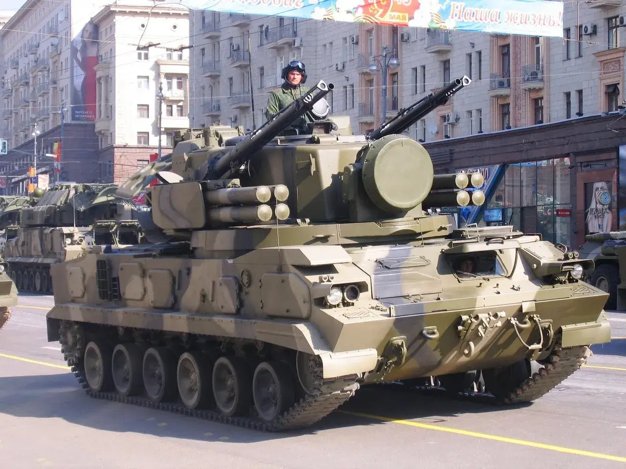Ein 2K22 Tunguska Flugabwehrpanzer fährt in einer Parade. Der Soldat im Turm trägt einen Helm und eine Uniform.