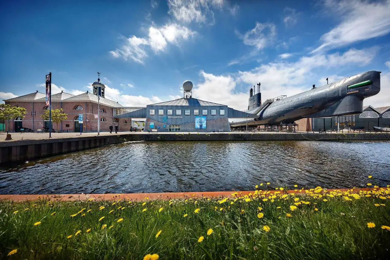 Das Den Helder Marinemuseum mit einem U-Boot vor der K&uuml;ste, umgeben von bl&uuml;henden gelben Blumen.