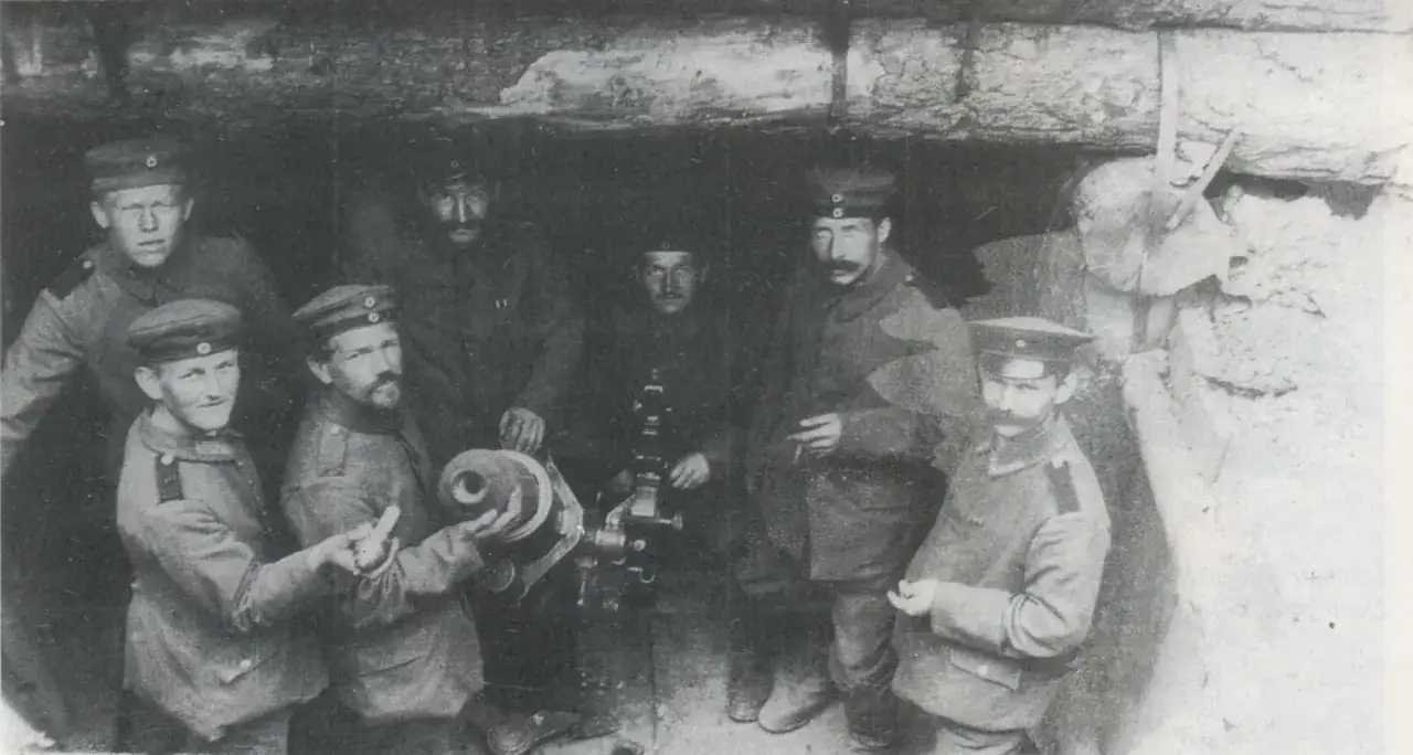 Soldaten posieren mit einem Minenwerfer im Graben. Der Mann rechts im Bild hält eine Granate.