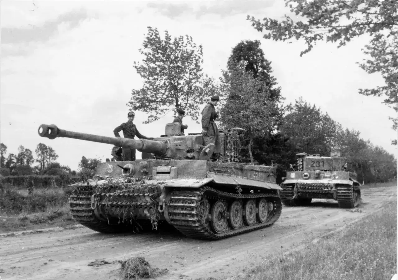 Besatzung auf einem Wittmann Panzer, der auf einer staubigen Straße steht. Ein weiterer Panzer mit der Nummer 231 im Hintergrund.