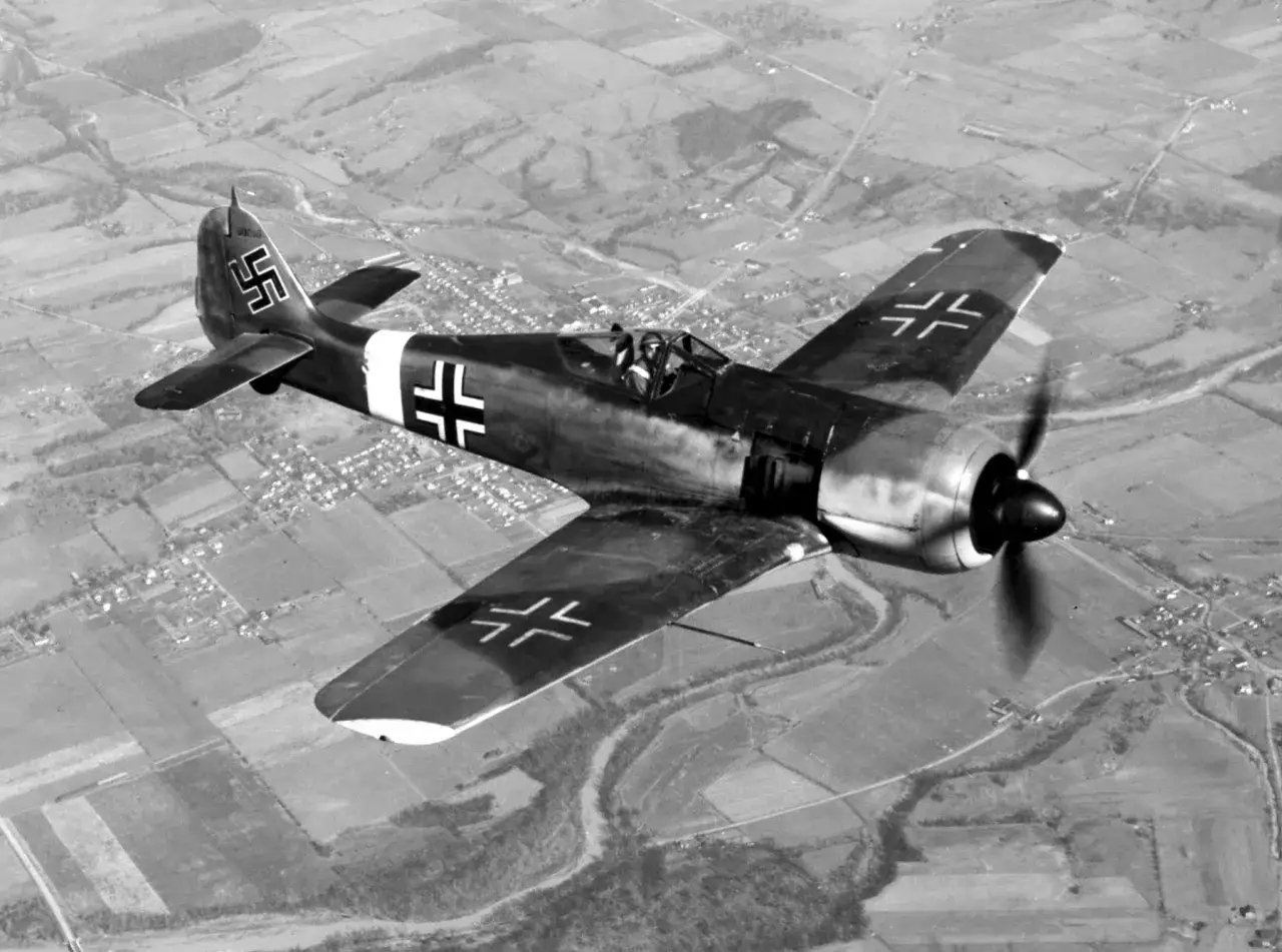 Ein Fw 190 A4 Jagdflugzeug fliegt über ländliches Gebiet.