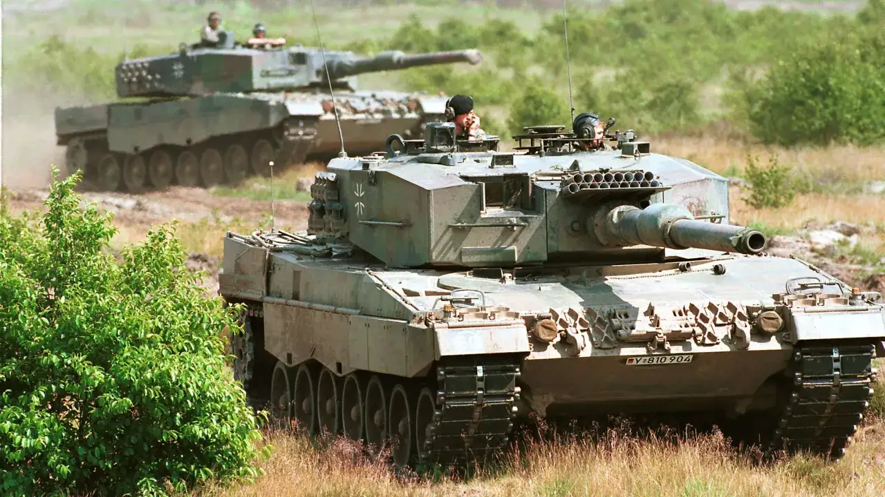 Zwei Leopard 1 Panzer fahren durch unwegsames Gelände. Der vordere Panzer ist nah und zeigt seine Besatzung.