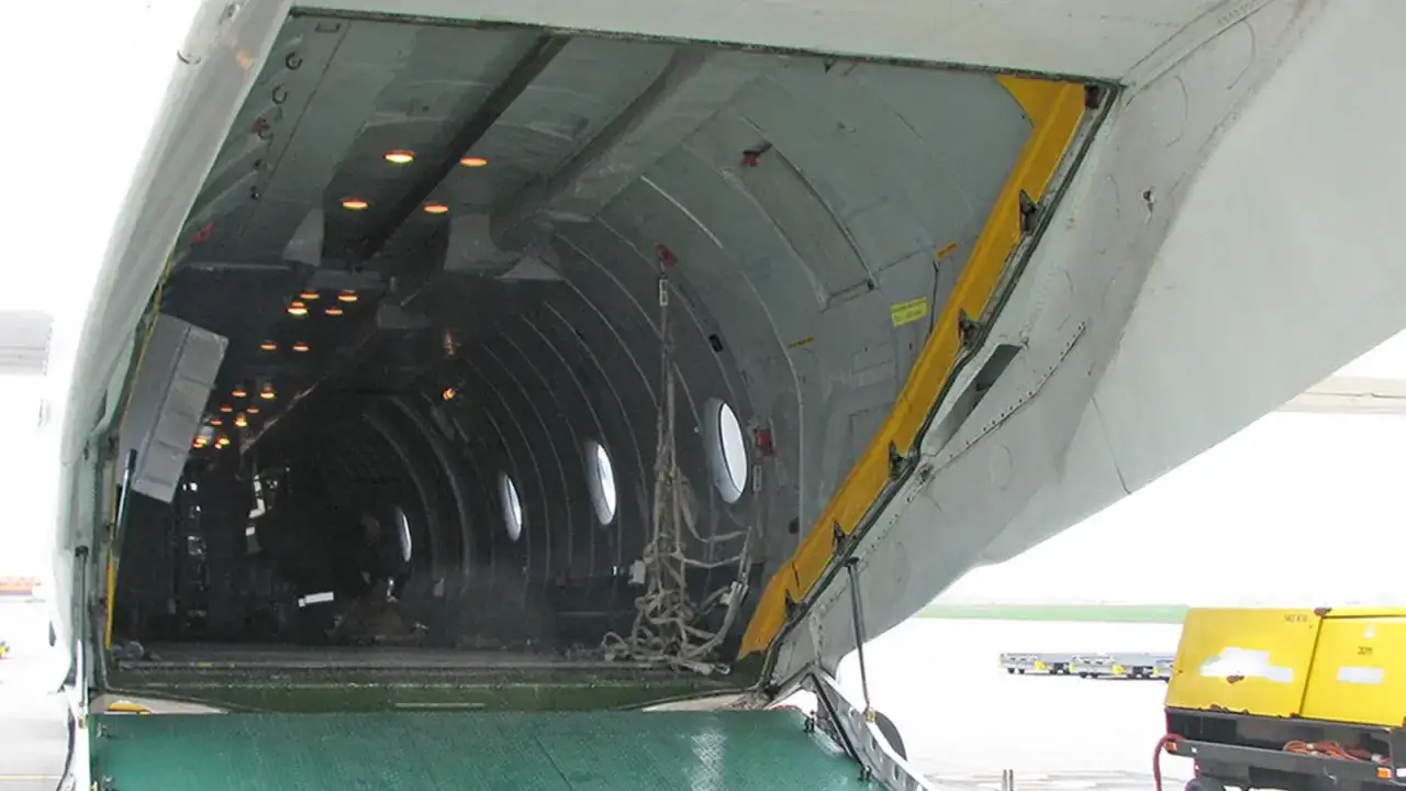 Das Innere eines Frachtflugzeugs vom Typ Antonov An-26b mit offener Heckrampe. Lichter beleuchten den dunklen Laderaum.