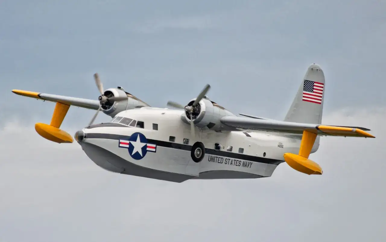 Grumman HU-16 Albatross, ein Wasserflugzeug der US Navy, fliegt mit gelben Schwimmern und Propellern im Himmel.