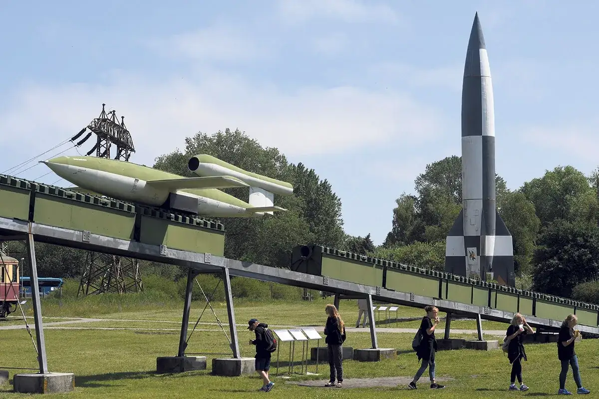 Eine V1-Flugbombe auf einer Startrampe und eine V2-Rakete, Zeugen deutscher Raketentechnik im 2. Weltkrieg, stehen im Freien.