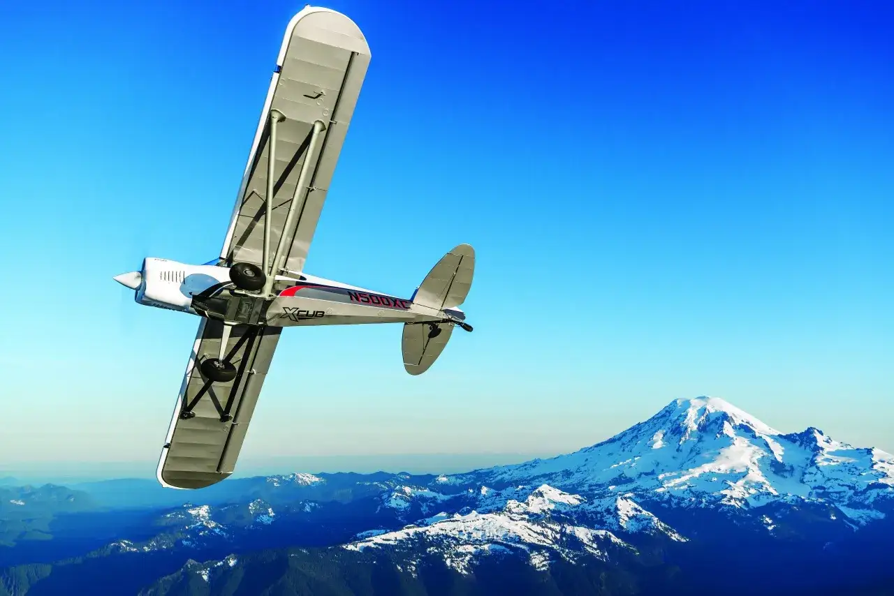 Ein CubCrafters X-Cub fliegt über schneebedeckte Berge.