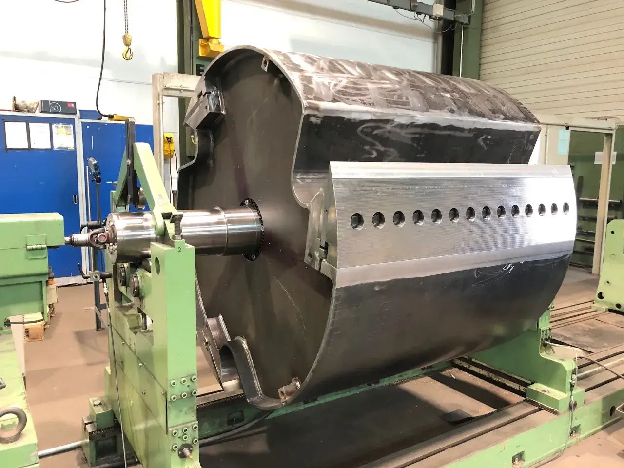 Großer Zylinder auf einer Maschine für dynamisches auswuchten. Die Maschine ist grün, der Zylinder ist metallisch und hat Schweißnähte.