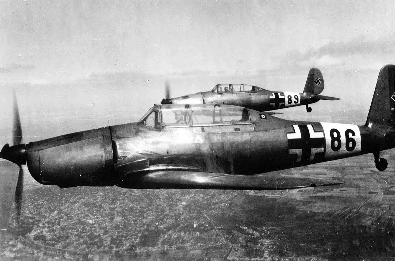 Zwei Arado 96 Flugzeuge fliegen über einer Stadt. Eines der Flugzeuge trägt die Nummer 86, das andere die Nummer 89.